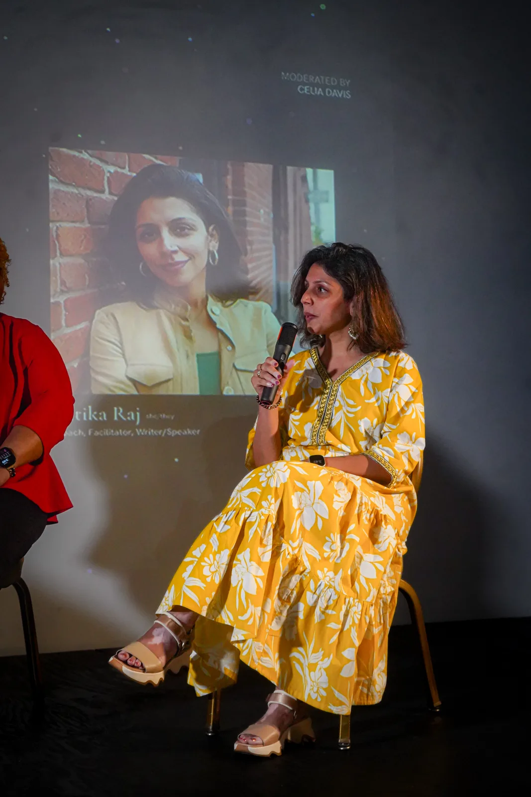A featured speaker in a yellow patterned dress addresses the Out of Office audience.